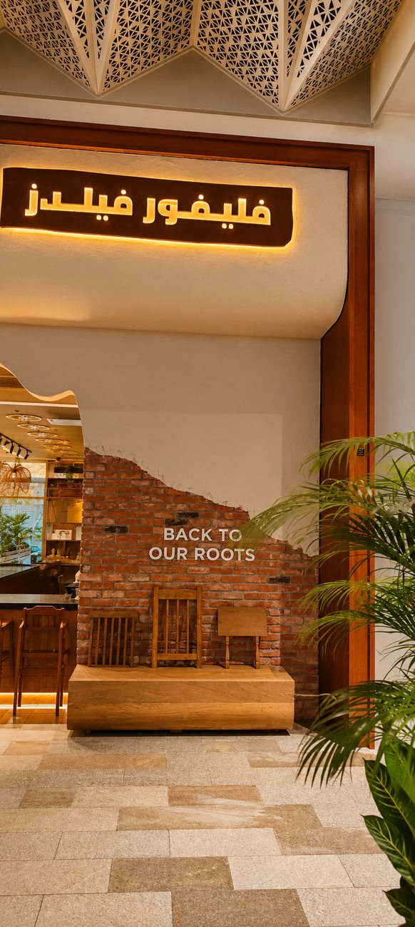 Flavour Fields entrance with illuminated Arabic signage and Back To Our Roots brick feature wall, Dubai Galleria Mall